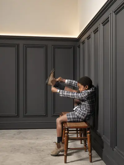 Zimmer mit dunklen Stuckleisten an der Wand in dem sich ein kleiner Junge Schuhe anzieht